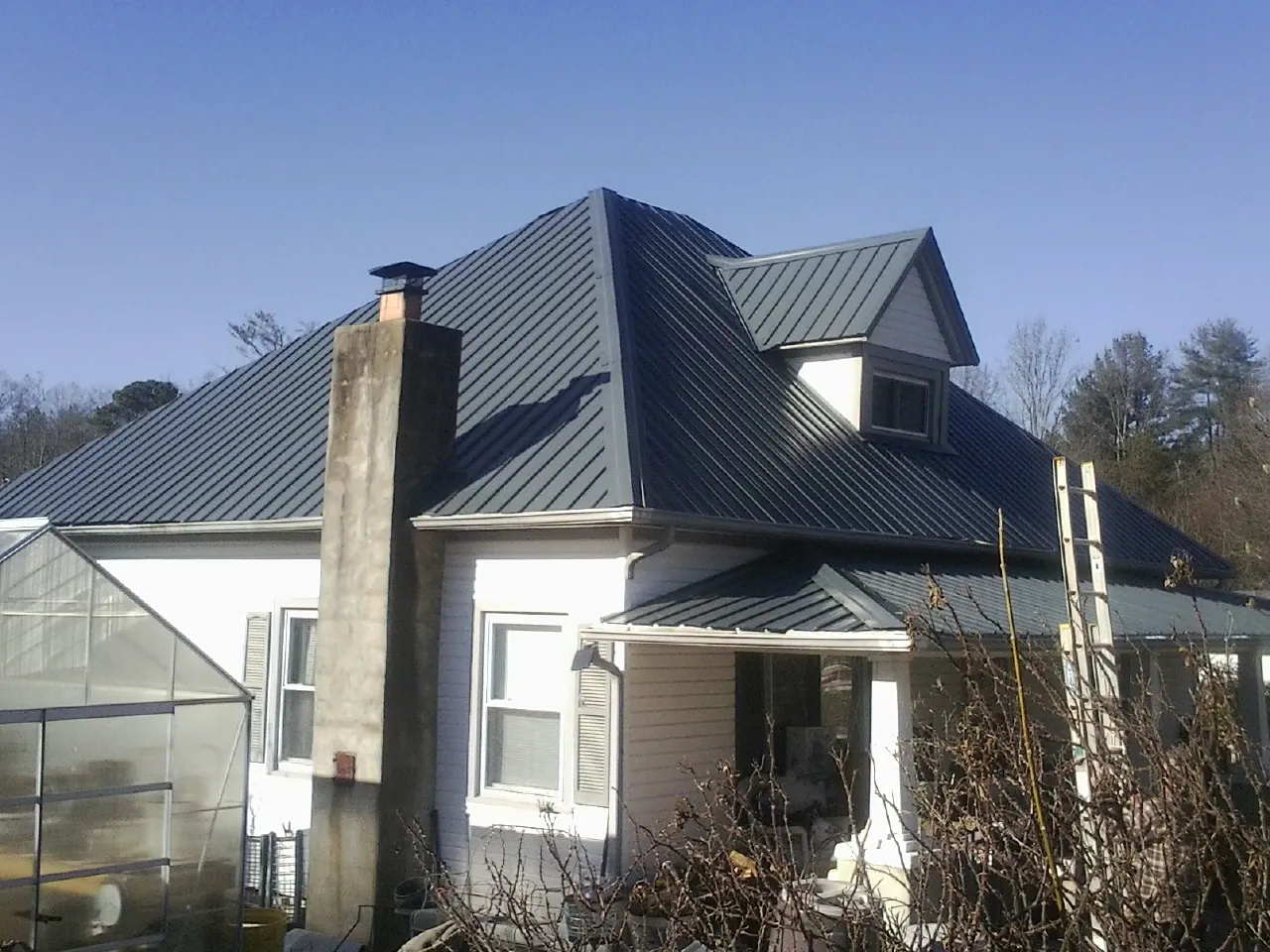 Dark blue standing seam metal roof on a white farmhouse with dormer — Slate & Tile Roof Repair by Roofing Brothers in Hustisford