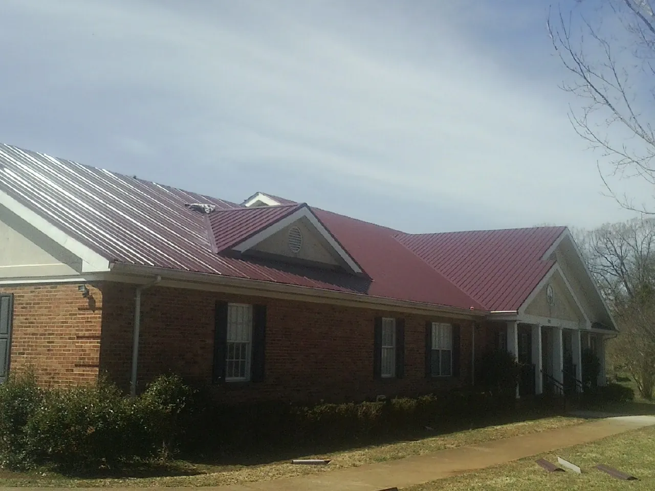 Red metal roof with gabled entries on a long brick building, from a Hail Damage Roof Repair job in Hustisford