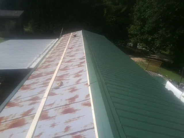 Old rusted panels beside newly installed green metal roofing — Wind Damage Roof Repair by Roofing Brothers in Hustisford