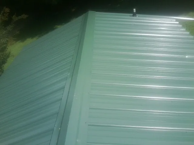 New green metal panels meeting at the ridge of a roof — Flat Roof Repair work by our crew in Hustisford