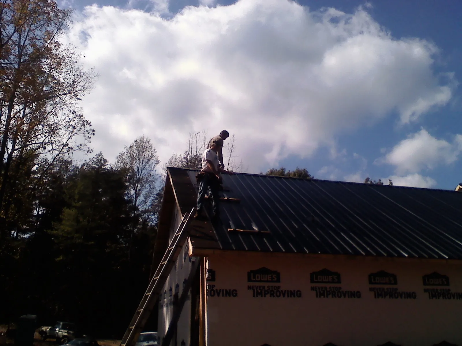 Roofer fastening dark metal panels high against a cloudy sky, from a Roof Inspection job in Hustisford