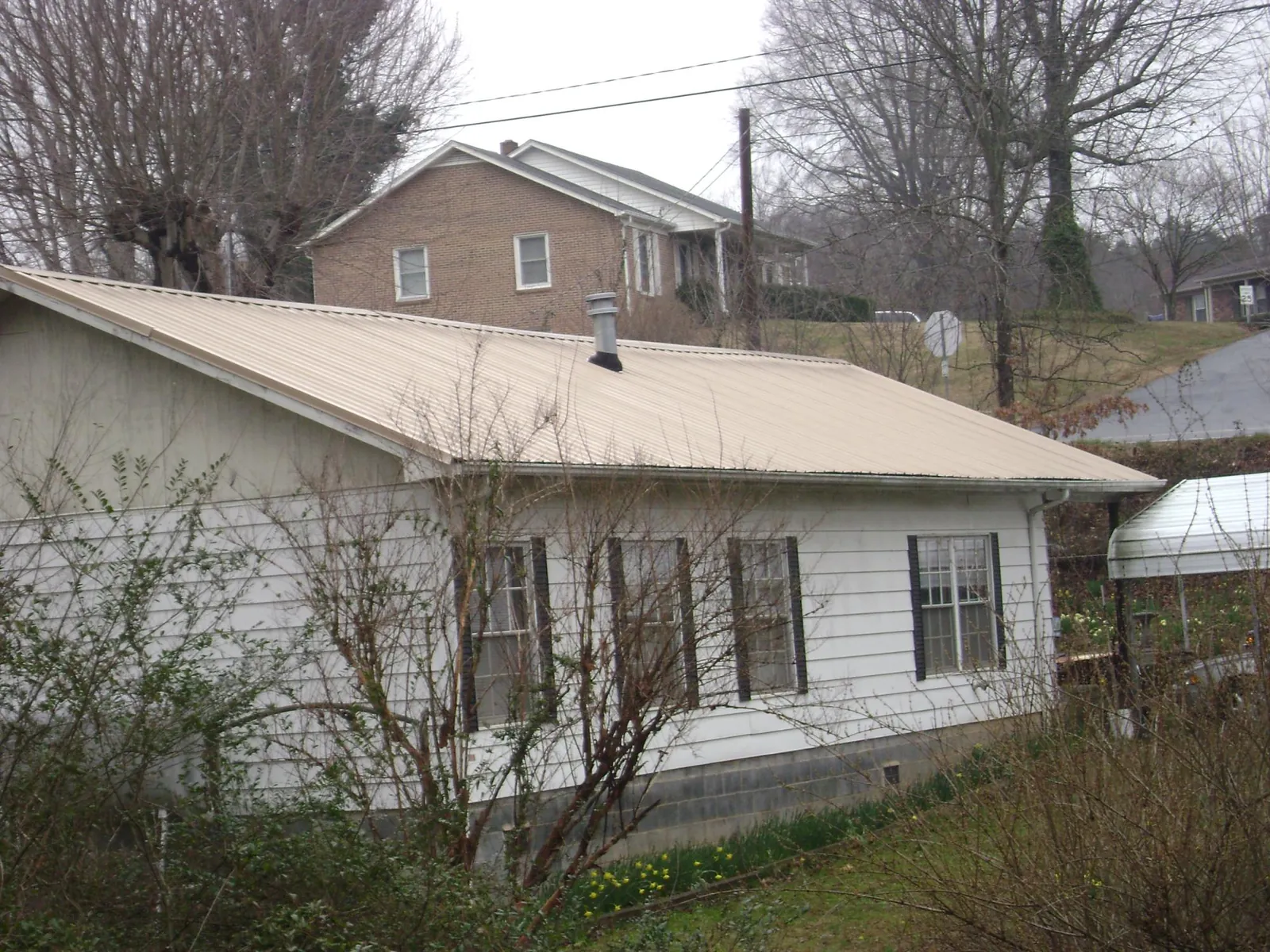 Tan metal roof on a white sided house set into a hillside — Commercial Roofing by Roofing Brothers in Hustisford